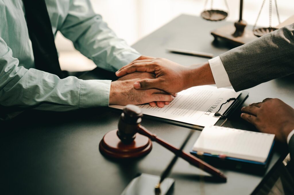 Two lawyers from All West Law Group shaking hands over a desk, symbolizing a successful agreement or partnership.