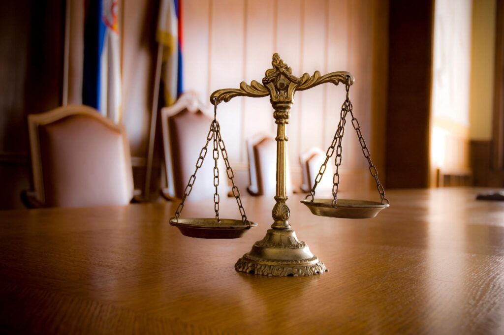A scale of justice rests on a wooden table, symbolizing law and fairness for All West Law Group.