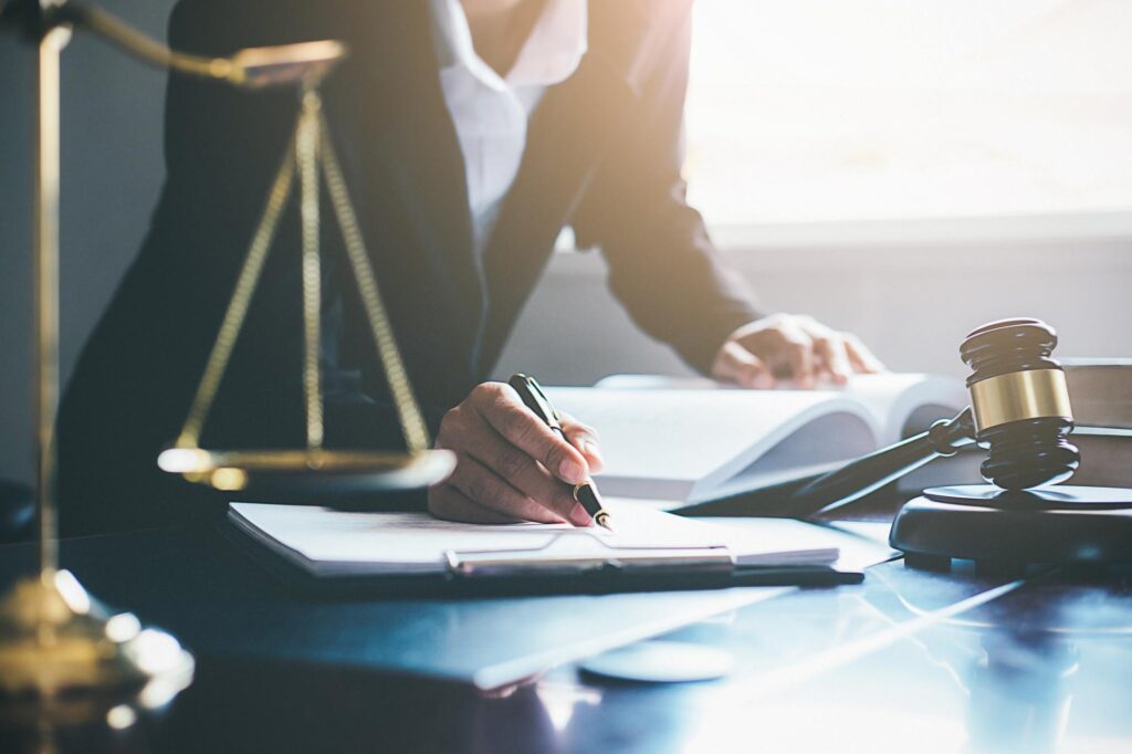 A person in a suit writes notes at a desk, surrounded by legal symbols such as scales of justice and a gavel, conveying a professional legal setting.