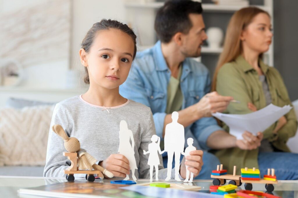 A young girl smiles while holding a colorful paper cutout of a family showcasing her creativity and imagination