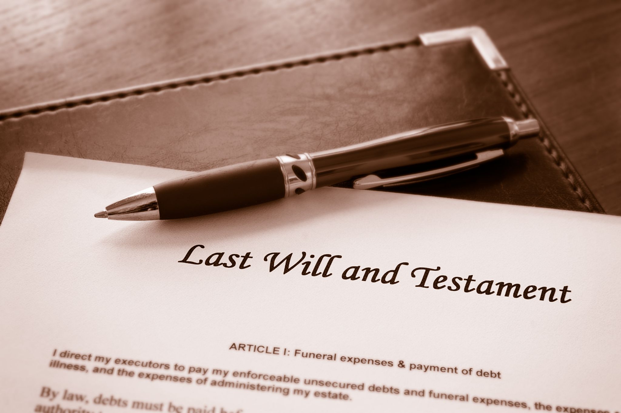 A close-up shot of a Last Will and Testament document with a pen resting across it on a leather folder.