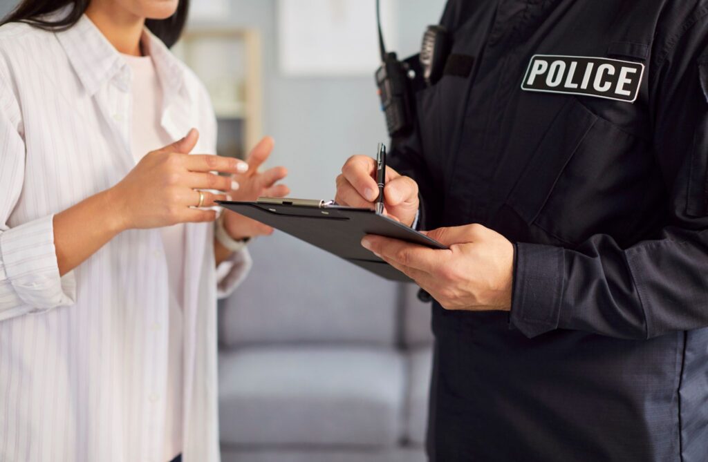 A police officer taking notes on a clipboard while talking to a woman gesturing with her hands.