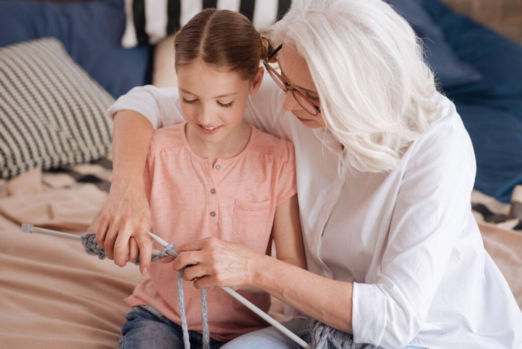 Grandmother and granddaughter smile while learning to knit together